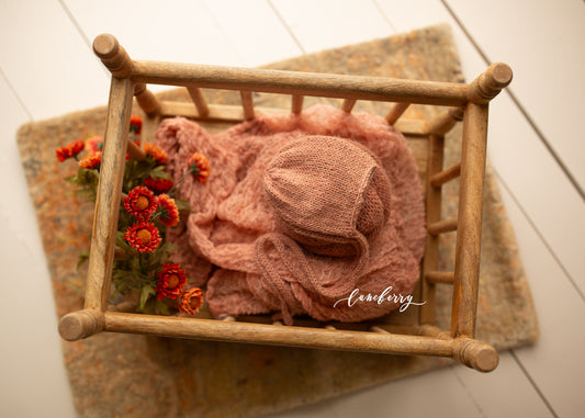 Peach set with a hat and blanket on a wooden crib, surrounded by flowers on a light wooden floor.